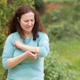 Woman scratching arm because it stings in a park with copy space