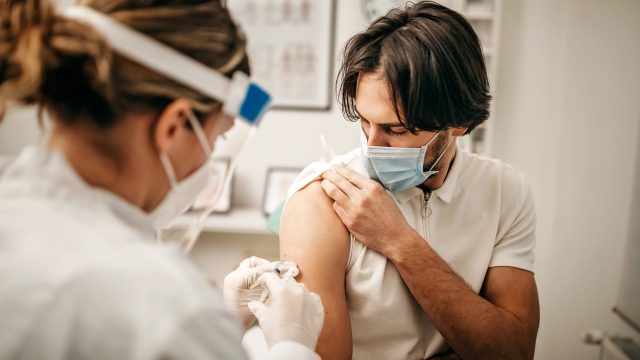 A young man rolling up his sleeve to receive a COVID vaccine booster shot