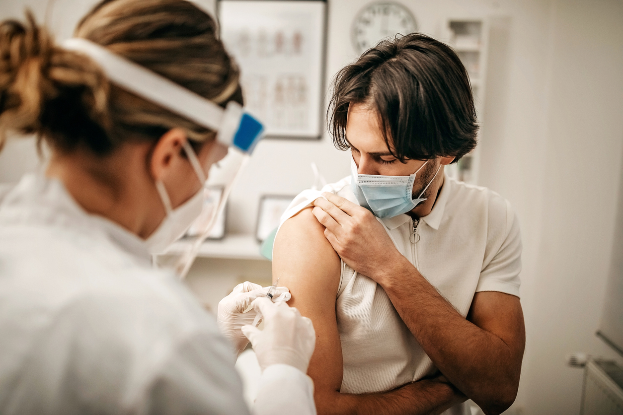 Un tânăr își suflecă mâneca pentru a primi o doză de rapel de vaccin COVID