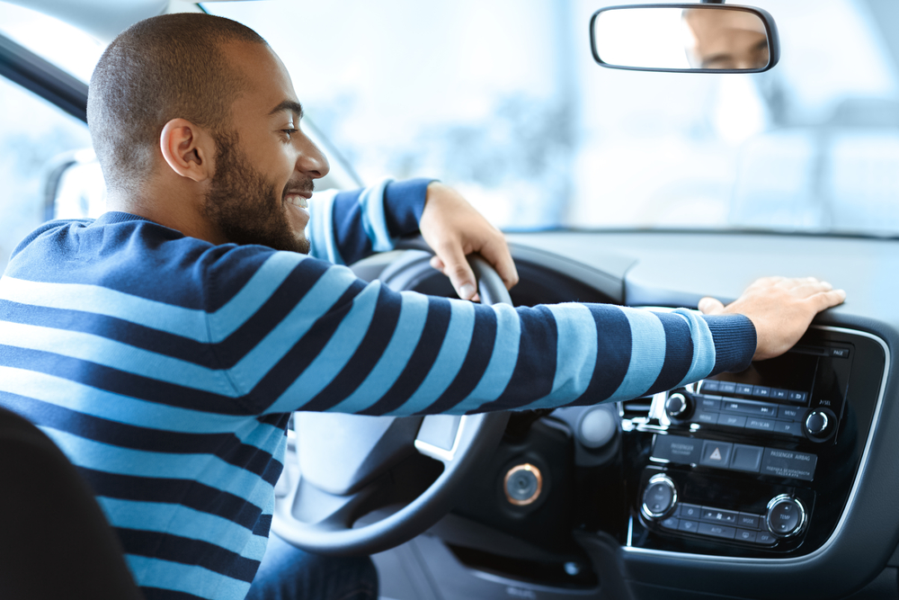 A man wearing a blue sweater sitting inside a car with a happy look on his face