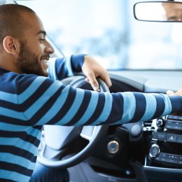 A man wearing a blue sweater sitting inside a car with a happy look on his face