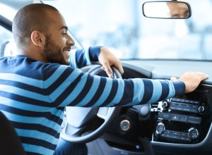 A man wearing a blue sweater sitting inside a car with a happy look on his face