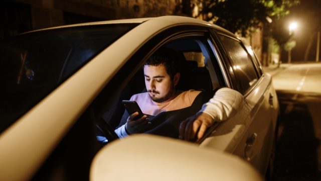A young man parked with his car looking at his smartphone
