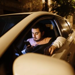 A young man parked with his car looking at his smartphone