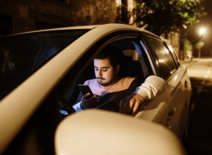 A young man parked with his car looking at his smartphone