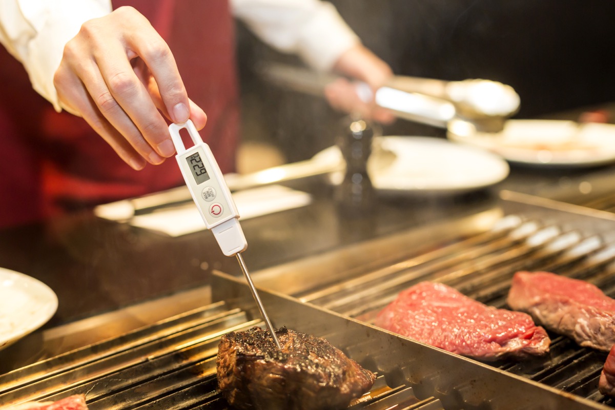 person using food thermometer to measure steak temperature
