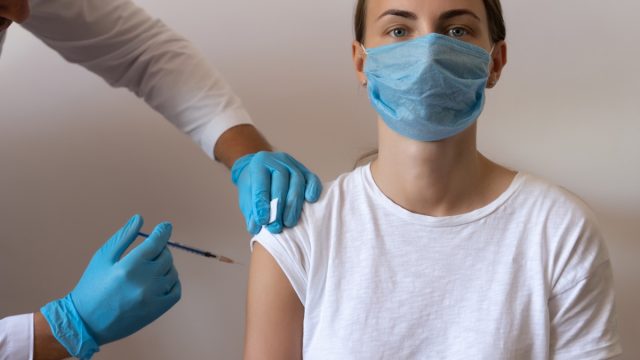 Woman and her doctor wearing face masks and getting a vaccine shot in a doctor's office. Doctor making injection to female patient in clinic.