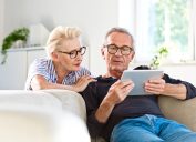 A senior man and woman look at a tablet while sitting on the couch