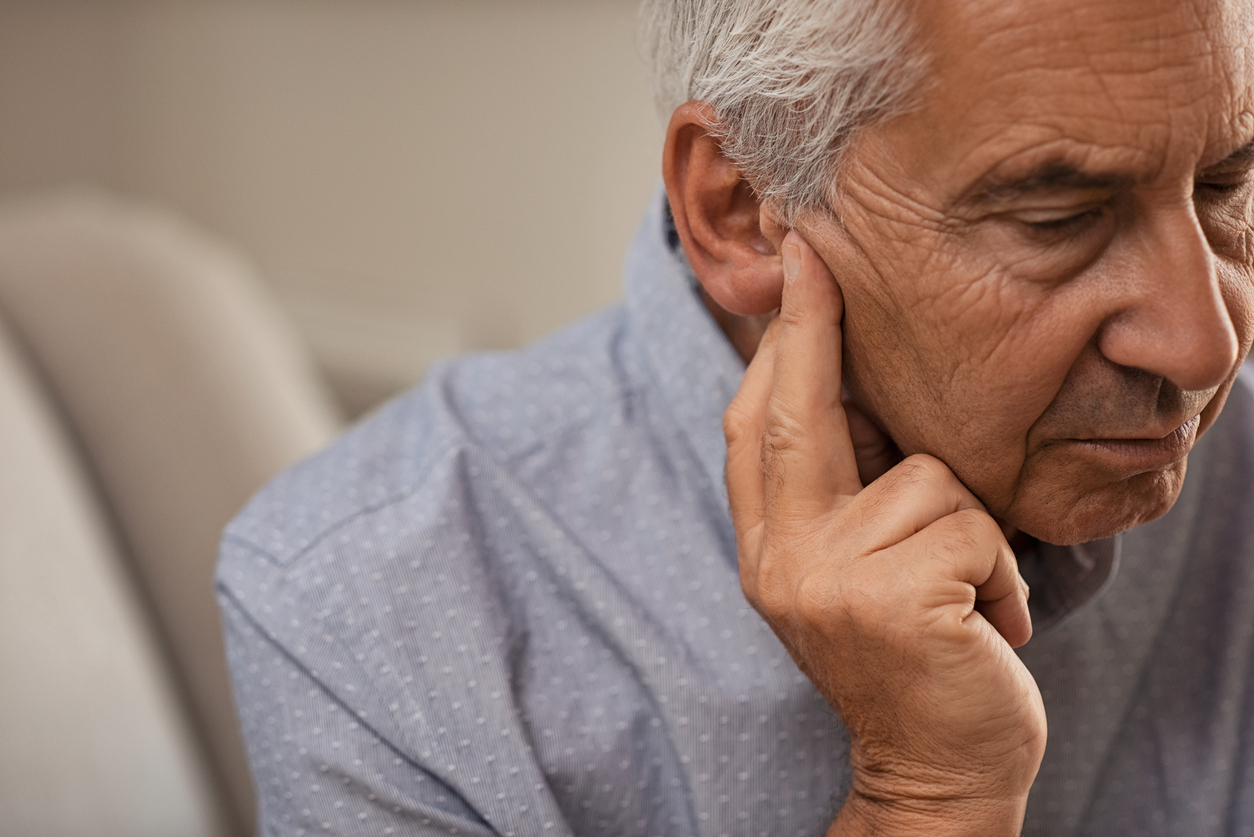Възрастен мъж, държащ ухото си, страдащ от увреждане или загуба на слуха