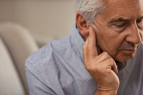 Alter Mann, der sein Ohr hält und an schwachem oder Hörverlust leidet