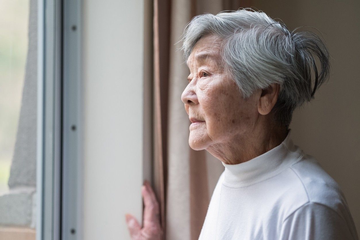 A senior woman looking out the window of her home