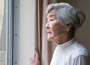 A senior woman looking out the window of her home