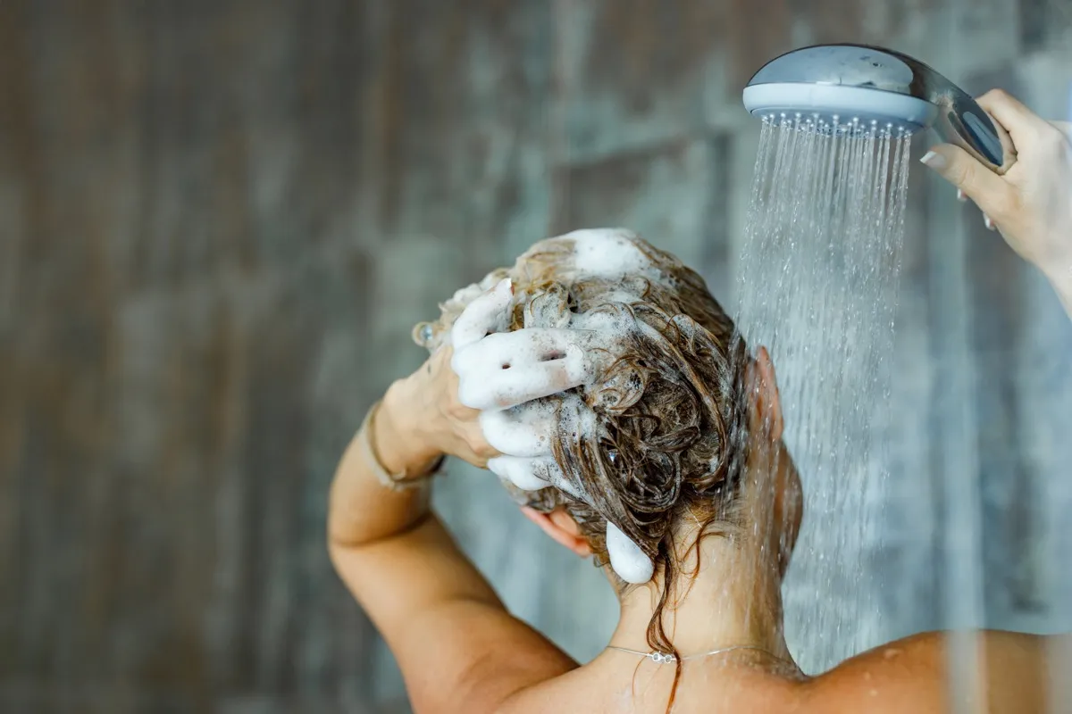 Vista trasera de una mujer lavándose el pelo con champú en el baño. Copie el espacio.