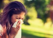 woman sneezing into a tissue outside