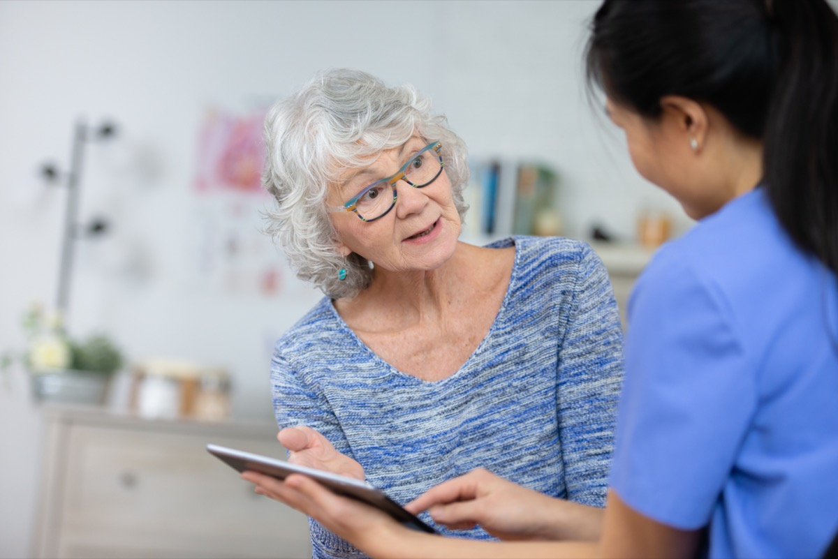 A senior woman speaks to her doctor about her health. She looks at her doctor after she explained to her what she needs to be healthy. The doctor is holding a tablet.