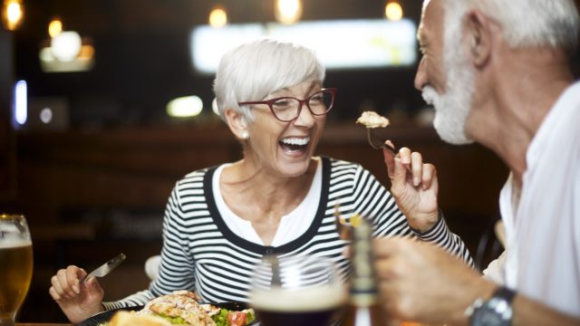 A senior woman feeding a senior man a bite of food during dinner at a restaurant