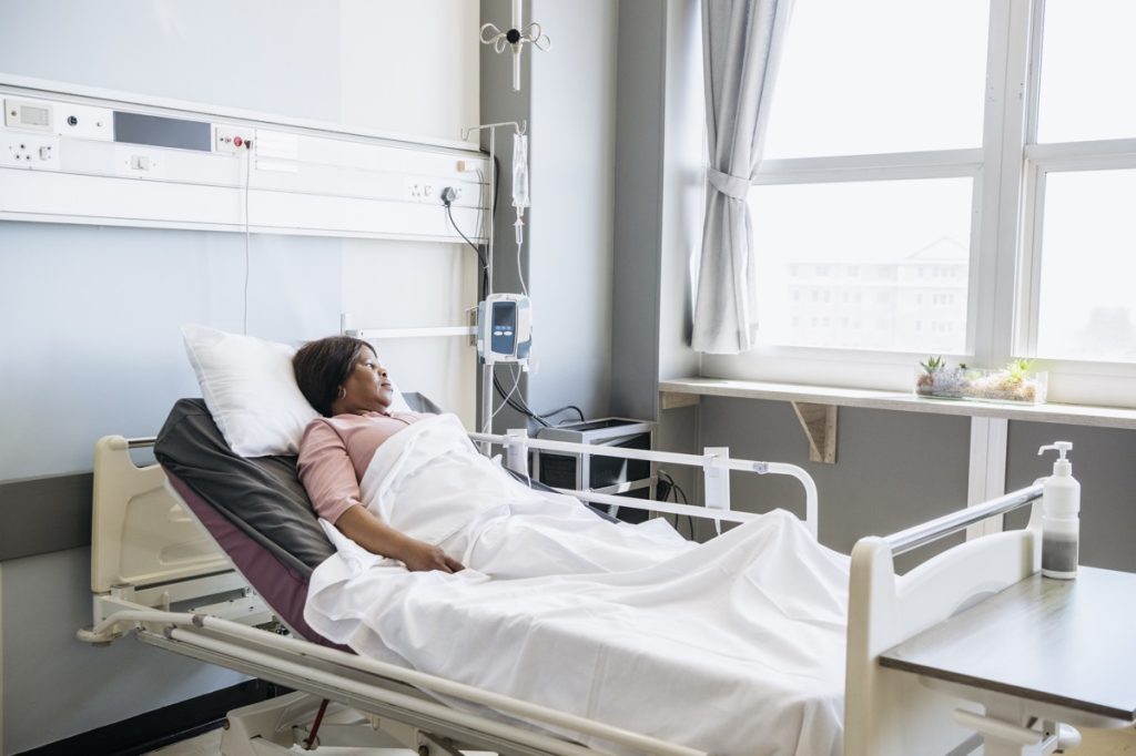 woman in her 50s with pensive expression, recovering on hospital ward, looking away and contemplating