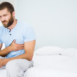 A young man sitting up in bed grabbing his chest with a pained look on his face