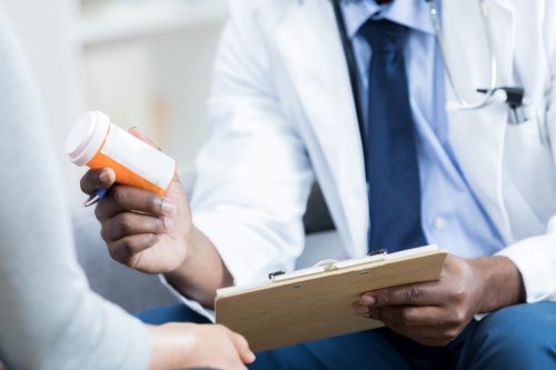 doctor hands a prescription medication bottle to a female patient. The doctor is holding the patient's chart.