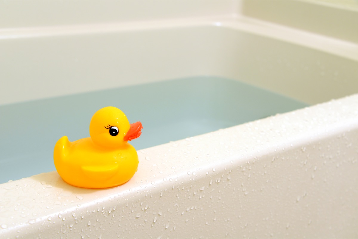 yellow rubber duck perched on ledge of bathtub