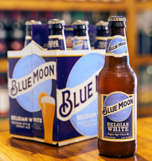 Blue moon beer bottle on wooden bar with out of focus pub background.