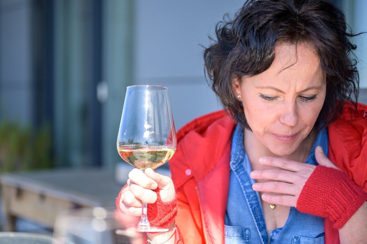 Woman coughing holding her hand to her chest with respiratory distress as she enjoys a glass of wine outdoors in a concept of symptoms of the coronavirus or Covid-19