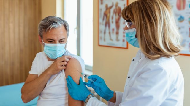 Vaccination, immunization, disease prevention concept. Mature Woman in medical face mask getting Covid-19 or flu vaccine at the hospital. Professional nurse or doctor giving antiviral injection to patient