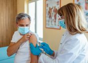 Vaccination, immunization, disease prevention concept. Mature Woman in medical face mask getting Covid-19 or flu vaccine at the hospital. Professional nurse or doctor giving antiviral injection to patient