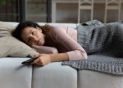 Tired millennial female relax at home after hard work day switch on favorite series
