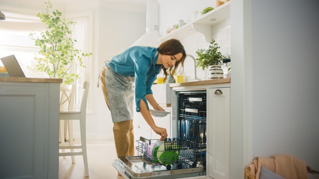 Woman loading a dishwasher without pre-rinsing dishes before