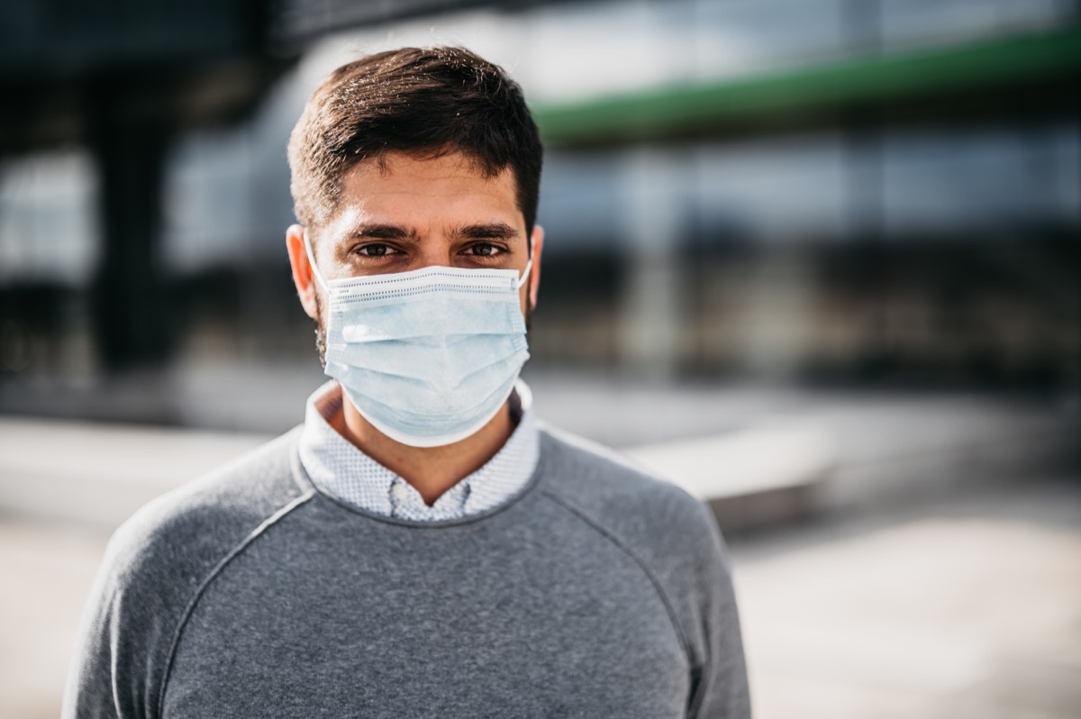 One young businessman with protective face mask standing outdoors in front of his office building.