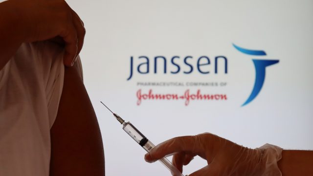 A close up of a gloved hand preparing to give someone a shot of vaccine with the Johnson & Johnson logo in the background