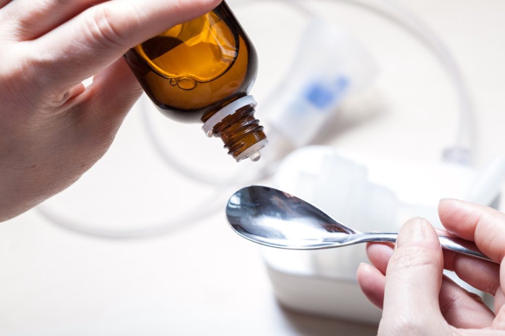 liquid medication pouring from amber bottle into spoon