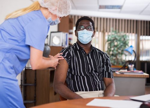 Ein junger Mann mit Gesichtsmaske erhält von einem Mitarbeiter des Gesundheitswesens einen COVID-19-Impfstoff