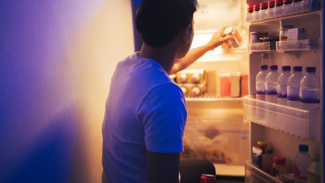Man is opening the refrigerator to get a soft drink during the night
