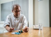 older man looking at bottles of prescription medication on wooden table