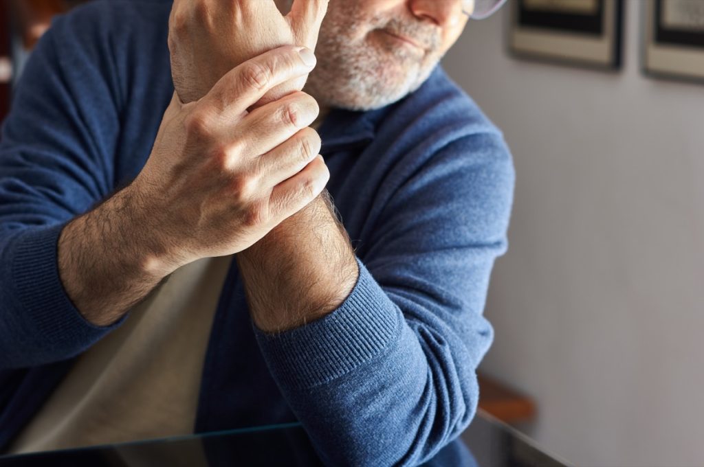 man sitting at home holding his left arm wrist due to pain caused by osteoarthritis, arthritis, tendonitis, rheumatism.