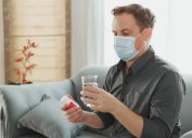 man looking at pill bottle while wearing surgical mask indoors
