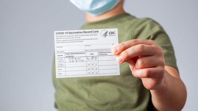 04-02-2021 Clarksburg, MD, USA: It is expected that kids will be getting vaccines before the start of the school year. Concept image showing a kid holding a COVID-19 vaccination record card