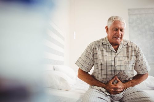 Sick senior man suffering from stomach ache holding his stomach in bedroom