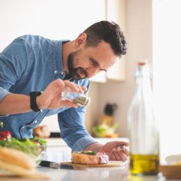 For better taste. Waist up portrait of handsome bearded gentleman in denim shirt seasoning raw beef steak