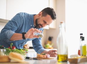 For better taste. Waist up portrait of handsome bearded gentleman in denim shirt seasoning raw beef steak