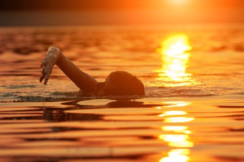 O persoană care înoată în ocean la răsăritul soarelui