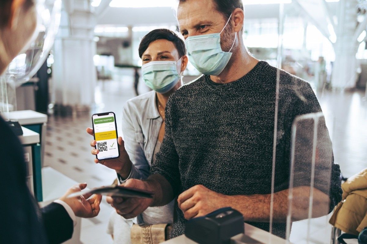 Tourist family showing vaccine passport at check-in counter at airport during pandemic. Man standing at check-in counter while woman showing digital vaccine passport to airline attendant