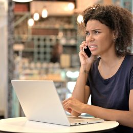 A young woman sitting in a cafe while answering a phone call with a confused look on her face