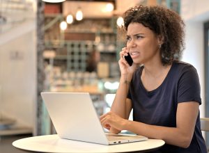 A young woman sitting in a cafe while answering a phone call with a confused look on her face