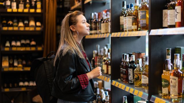 Woman in a liquor store looking at a shelf with bottles of whiskey.