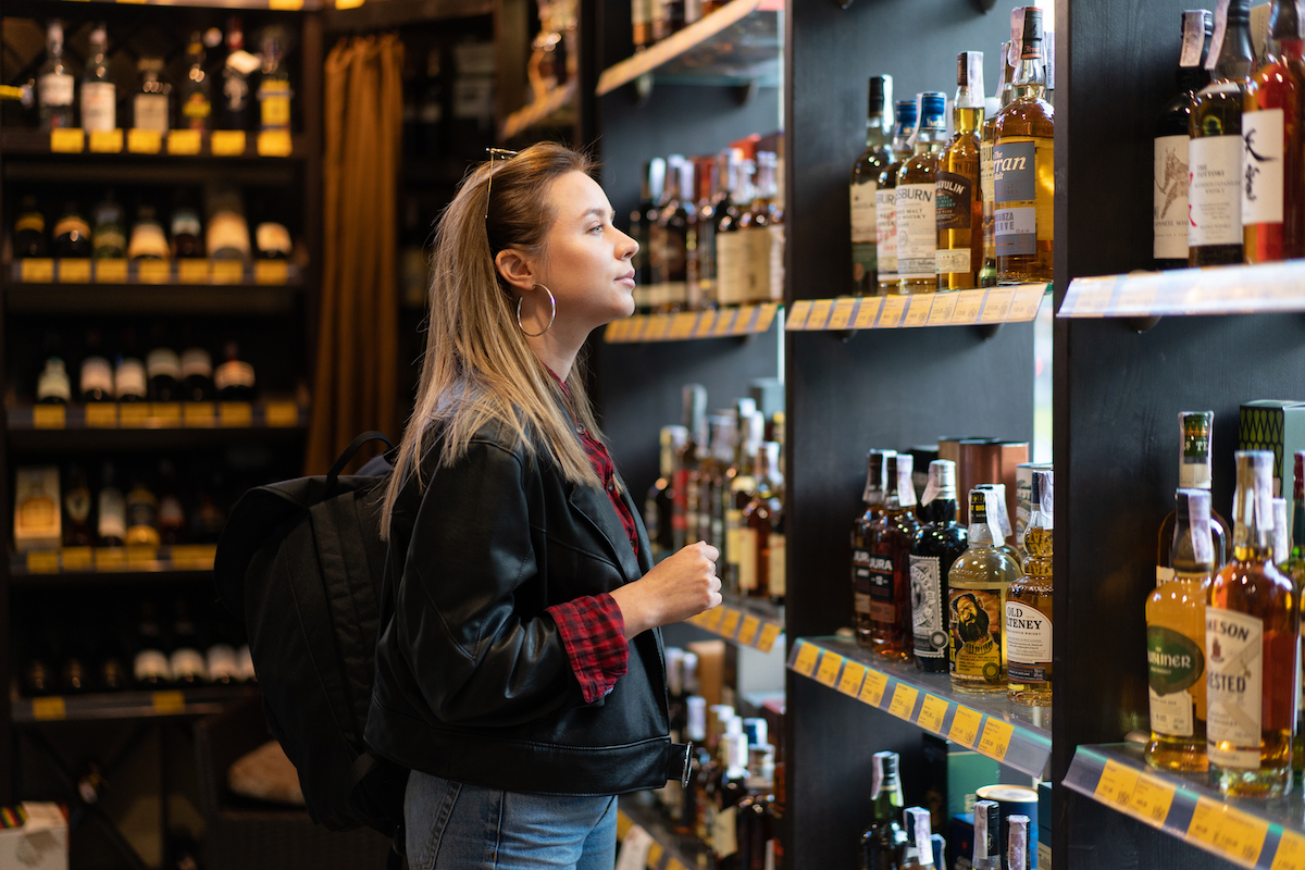 Woman in a liquor store looking at a shelf with bottles of whiskey.