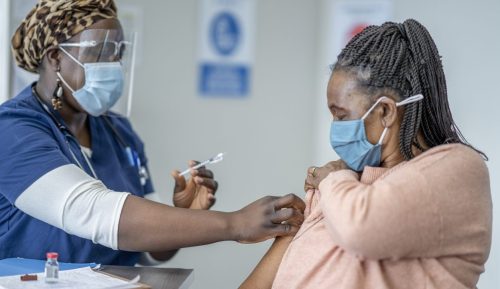 Eine Frau mittleren Alters erhält von einem Mitarbeiter des Gesundheitswesens einen COVID-19-Impfstoff