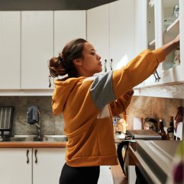 A young woman reaching inside a kitchen cabinet